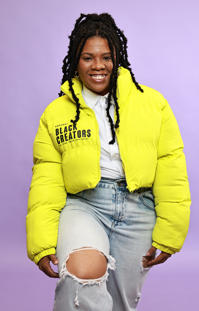 Sade Wilkins in a yellow jacket smiling at the camera for her A is for Art profile photo